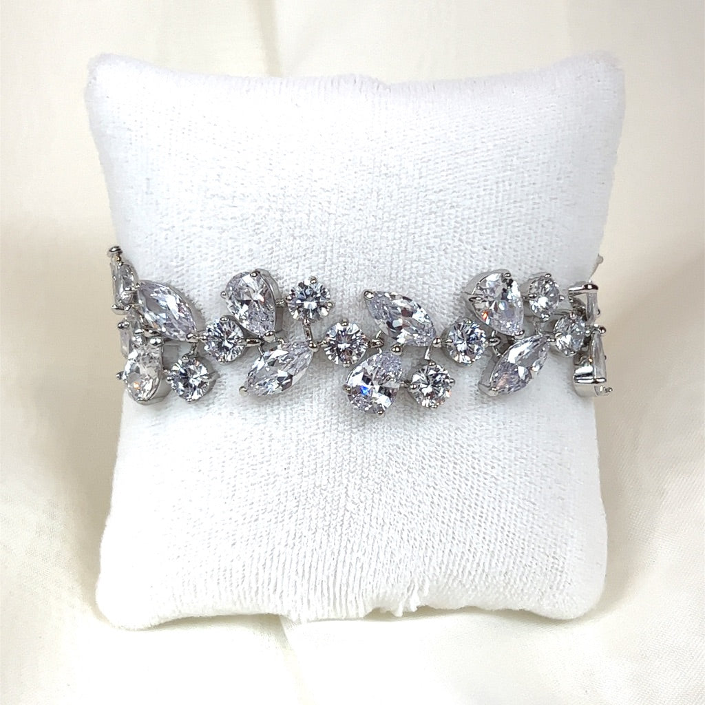 The Bold Branchy Wedding Bracelet (style no. B140), features clear round and teardrop Cubic Zirconia stones forming elegant floral and leaf patterns, reminiscent of a Swarovski crystal bridal tiara, is displayed on a small white cushion against a neutral background.
