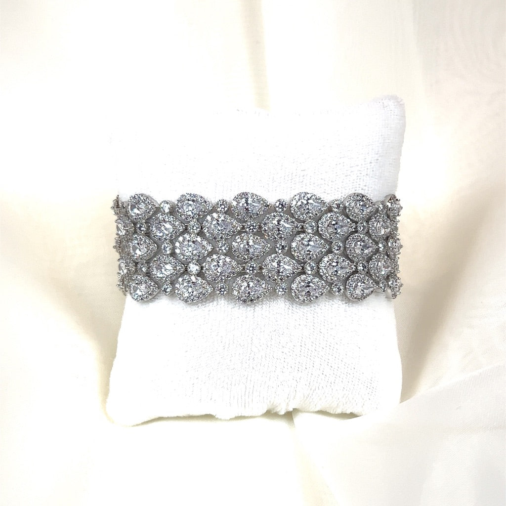 A sparkling silver Layered Classic Teardrop Bracelet (style no. B150), adorned with numerous diamond-like stones, reminiscent of a Swarovski headband, is displayed on a white cushioned stand.