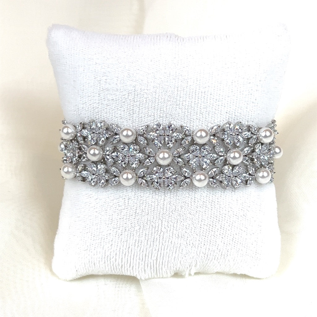 The Cuff Blossom Bracelet (style no. B145) is a sparkling bridal bracelet featuring intricate floral patterns, pearls, and small cubic zirconia diamonds. Displayed on a white cushion.
