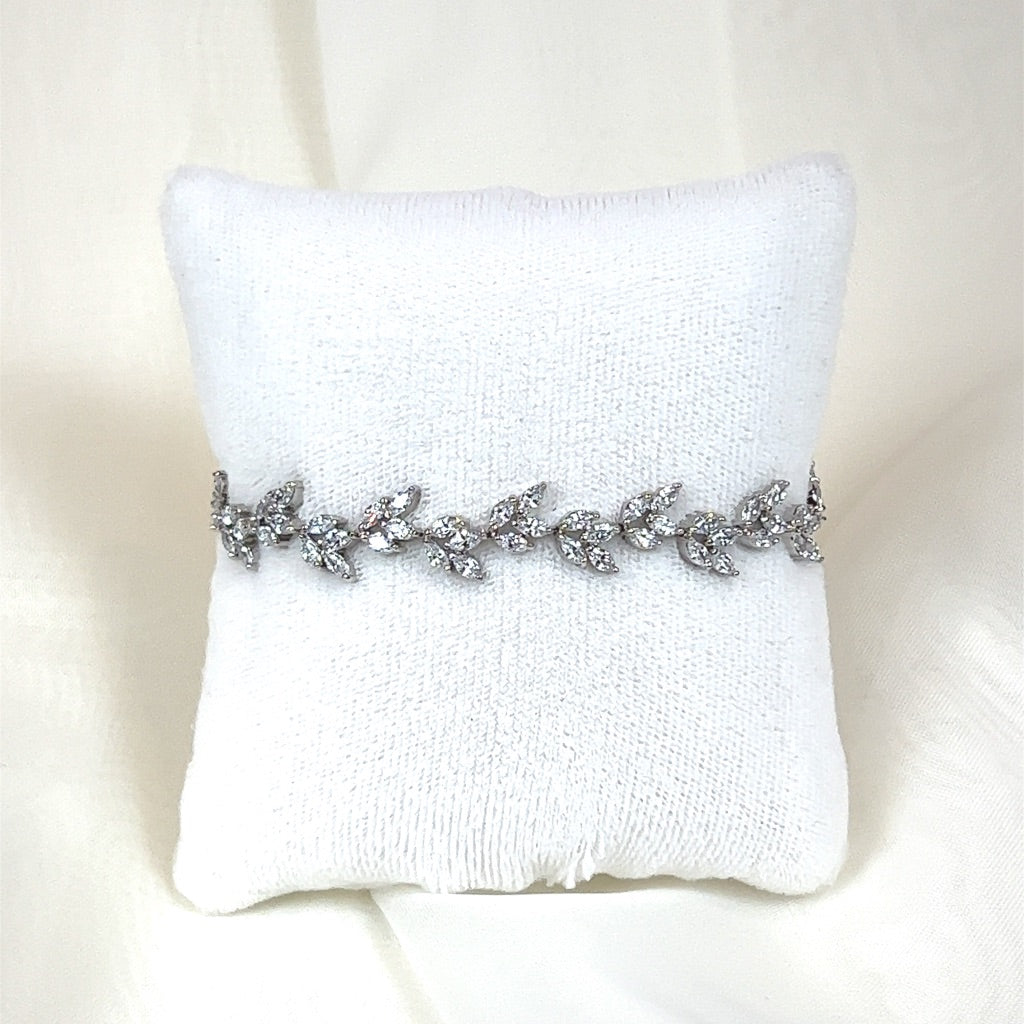 The Olive Branch Bracelet (style no. B144) features intricate leaf-shaped designs set with sparkling stones, elegantly displayed on a white pillow—a perfect match for a Swarovski crystal crown or bridal hair combs on a soft, light background.