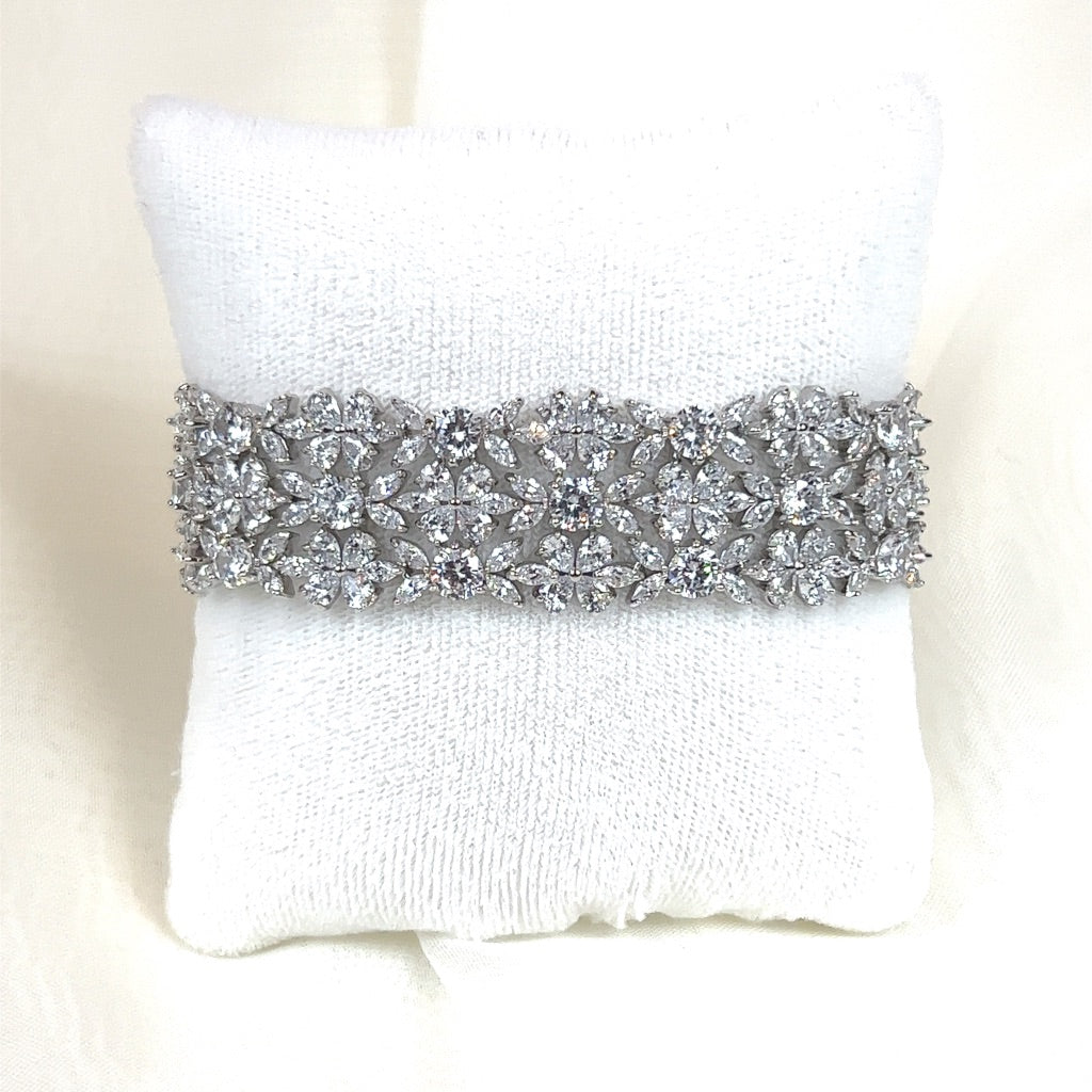 The Cuff Blossom Bracelet (style no. B145) is a sparkling silver piece with intricate floral and star designs, resting on a white cushion, reminiscent of a Swarovski bridal tiara. It features numerous small, clear gemstones for a shimmering effect.