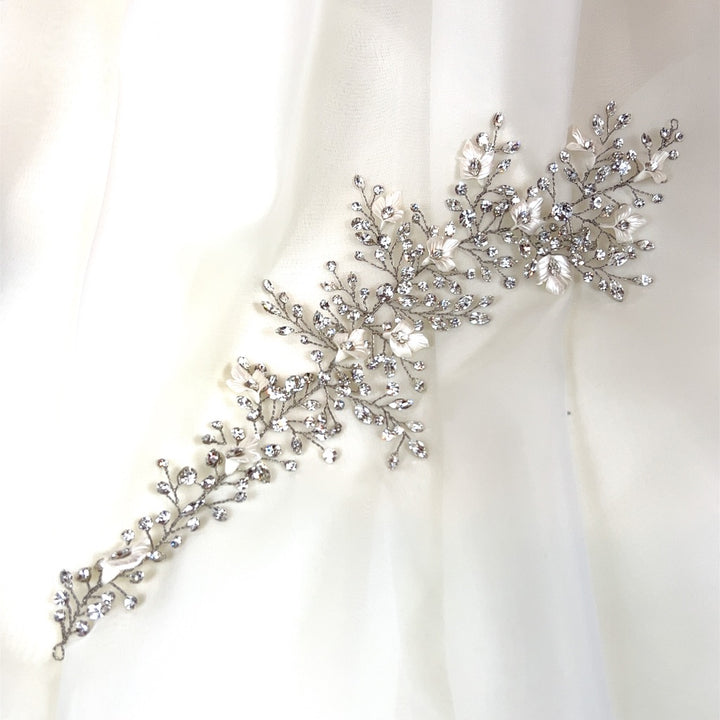 The Crystal and Flower Branch Vine, style no. 242736, is a delicate Swarovski crystal bridal hair accessory featuring floral and leaf designs with sparkling crystals. It is elegantly displayed on a soft white fabric background.